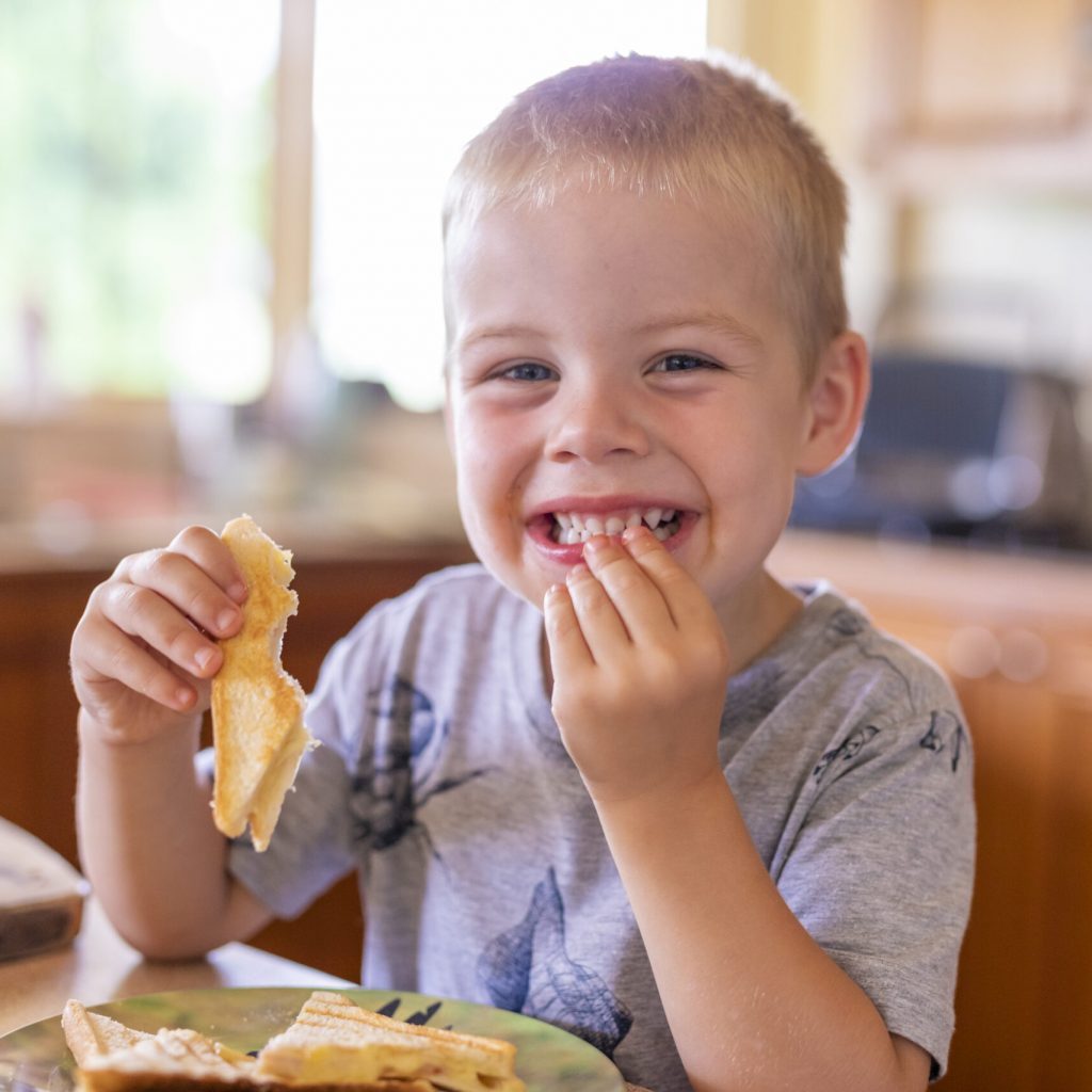 Happy Young Boy Eating Lunch in the Kitchen Happy Young Boy Eating Lunch in the Kitchen